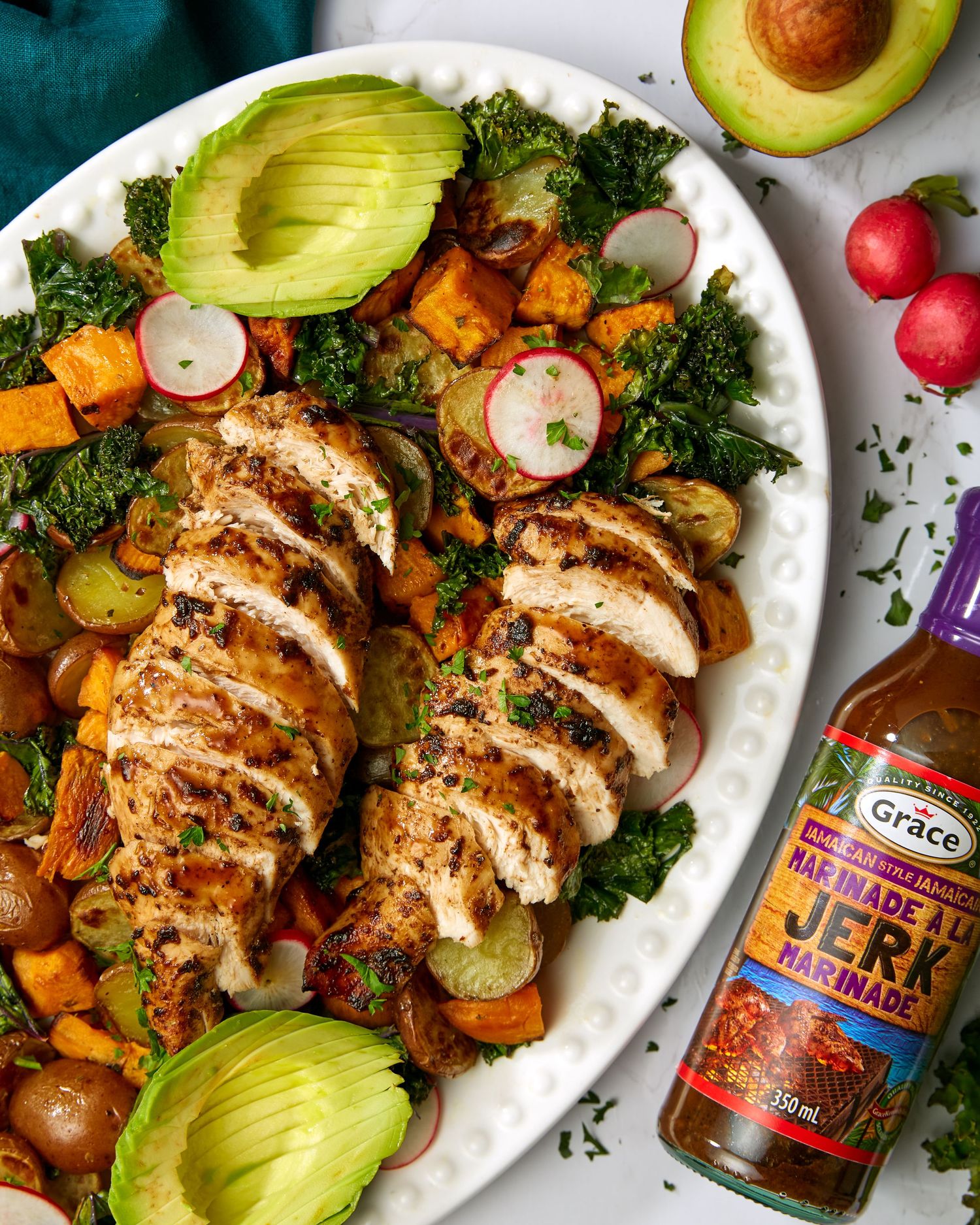 Grilled chicken breast with avocado, roasted sweet potatoes, radishes and fresh herbs on a white plate.
