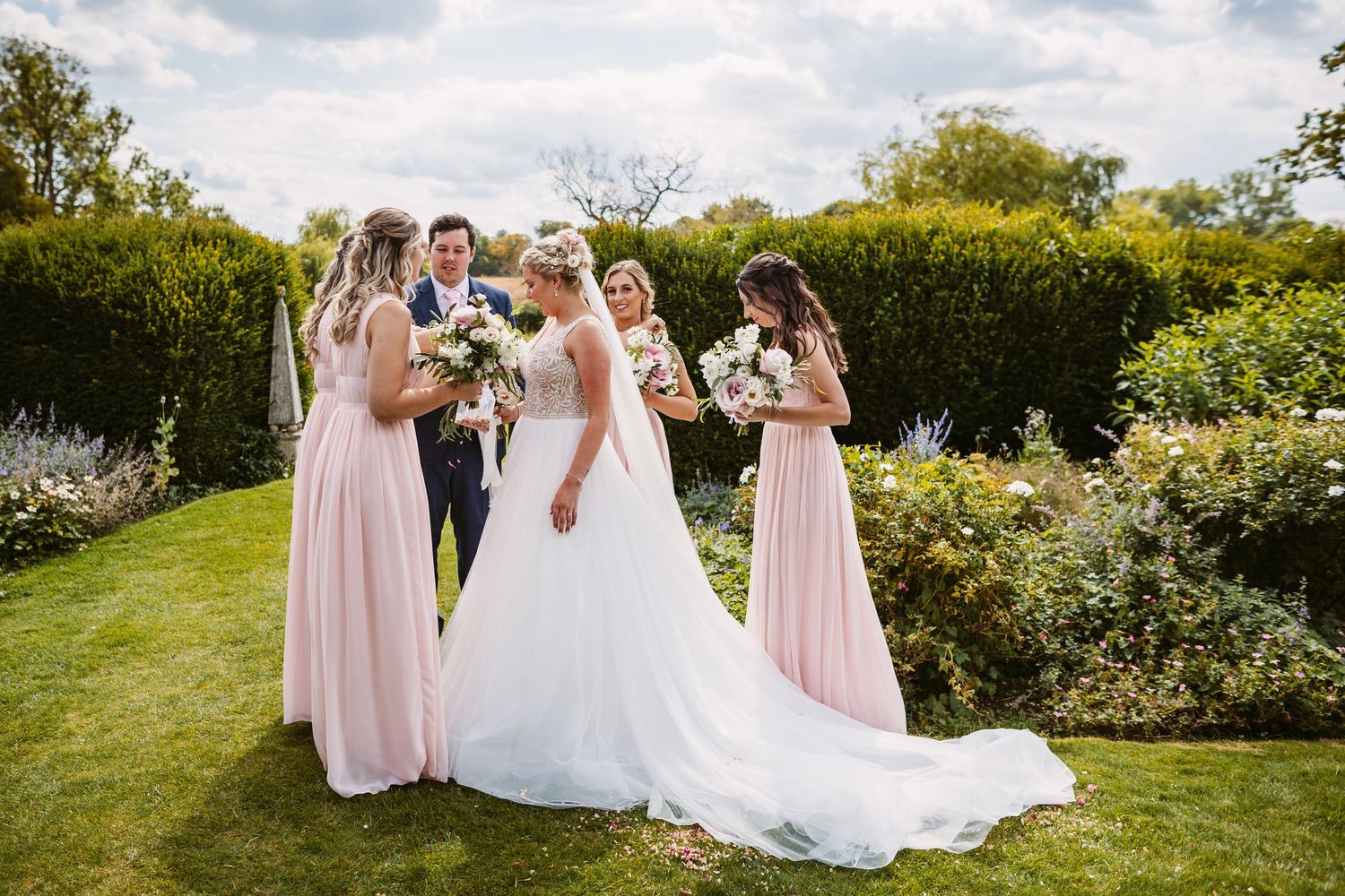 Bridal party in pink dresses gathered on a manicured lawn.