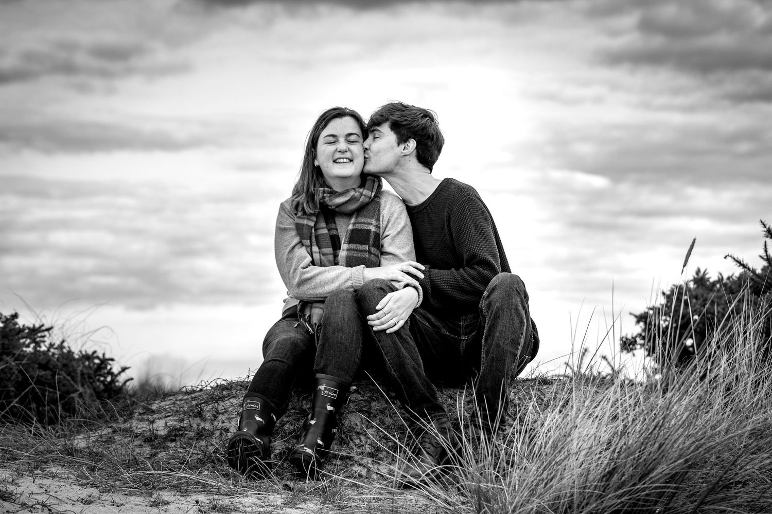 Couple sharing intimate moments on a grassy hilltop during sunset.