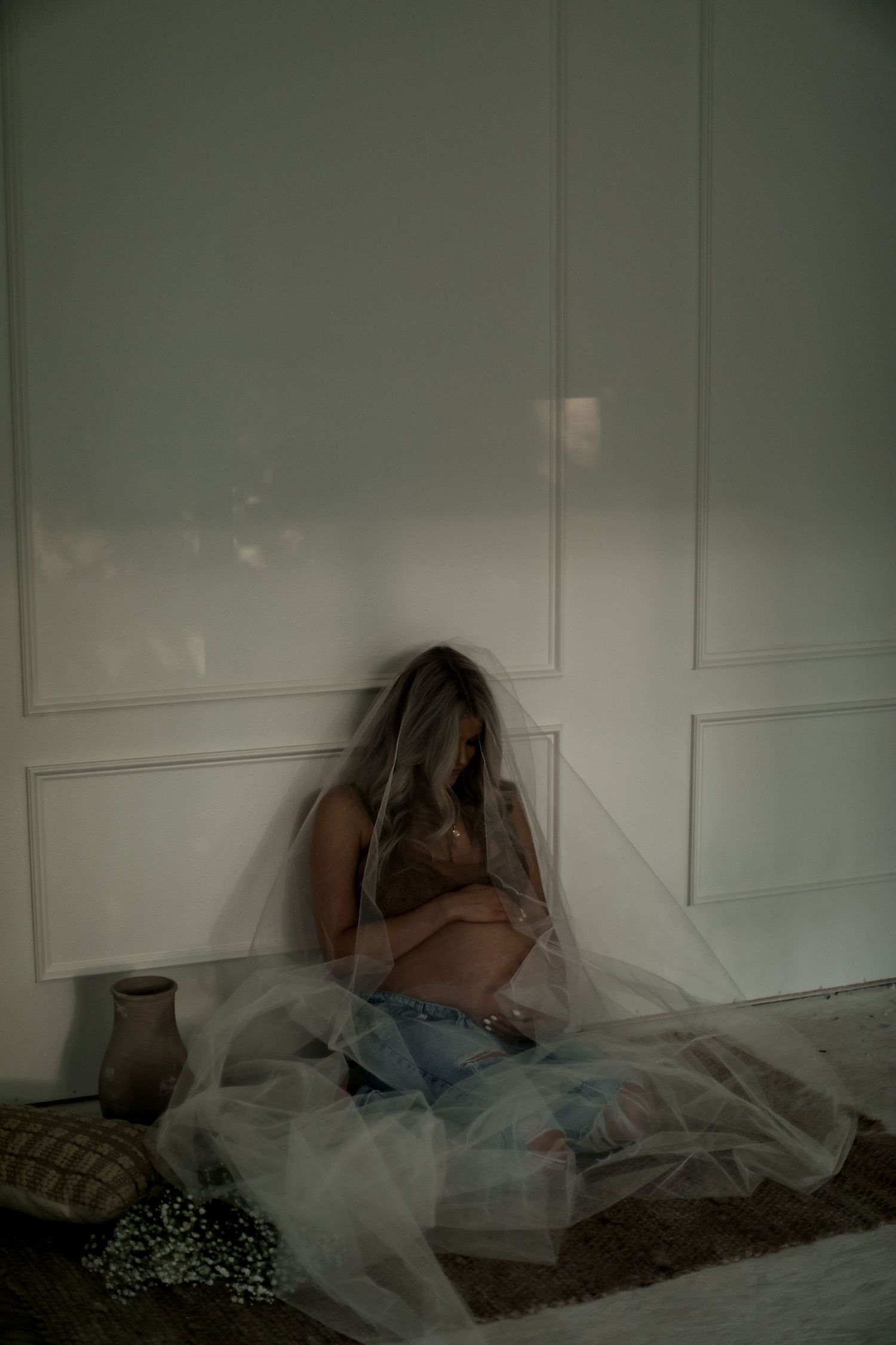 Moody maternity scene with tulle fabric and soft lighting in a corner.