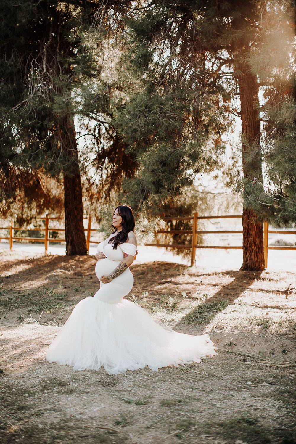 A beautiful white wedding dress flows in a sunlit forest setting with tall pine trees and dappled light.