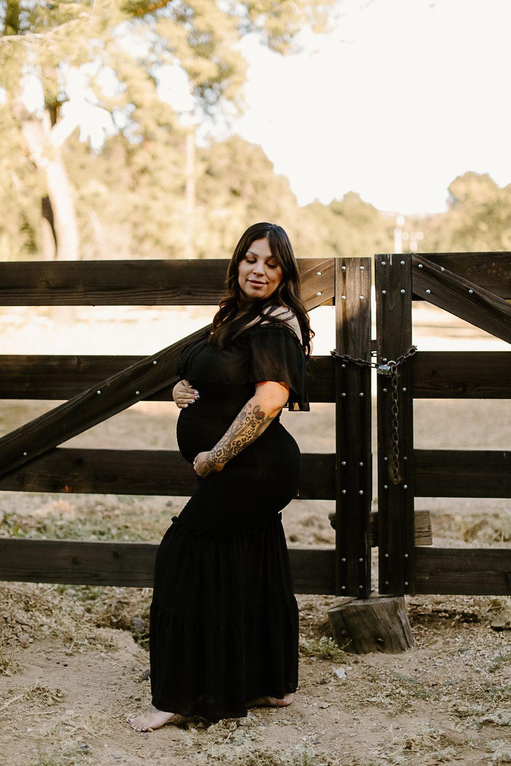 Artistic maternity photos in black dress against wooden fence.