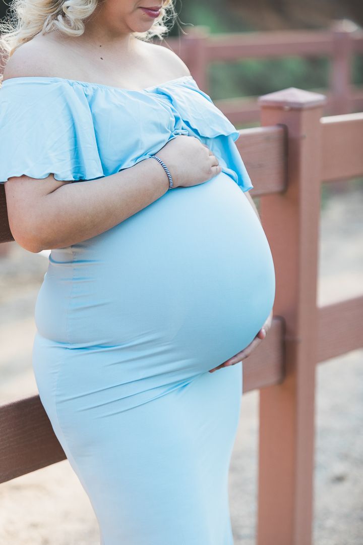 Close-up maternity photos showing pregnant belly in light blue off-shoulder dress.