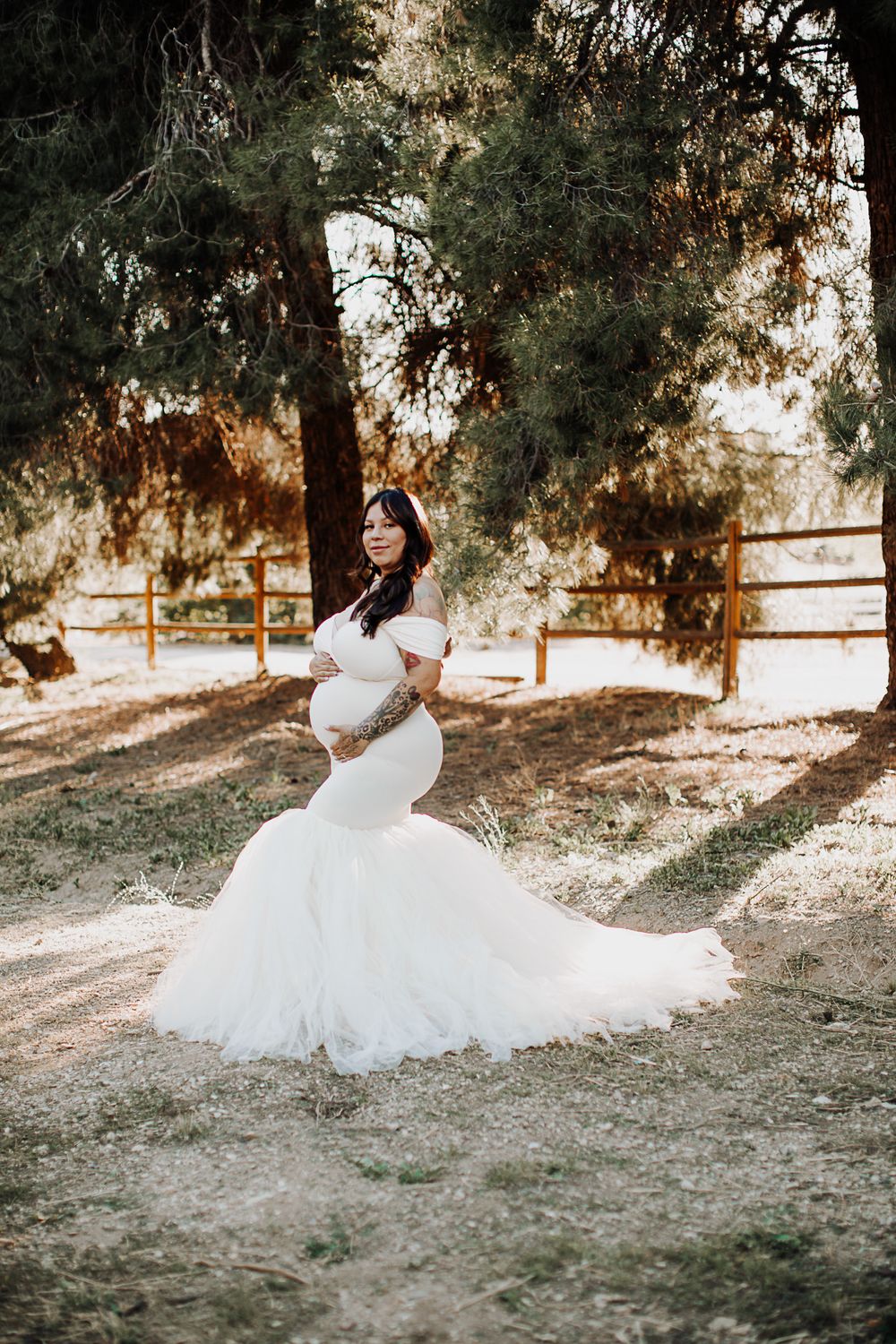 Ethereal maternity portraits in white gown among pine trees.