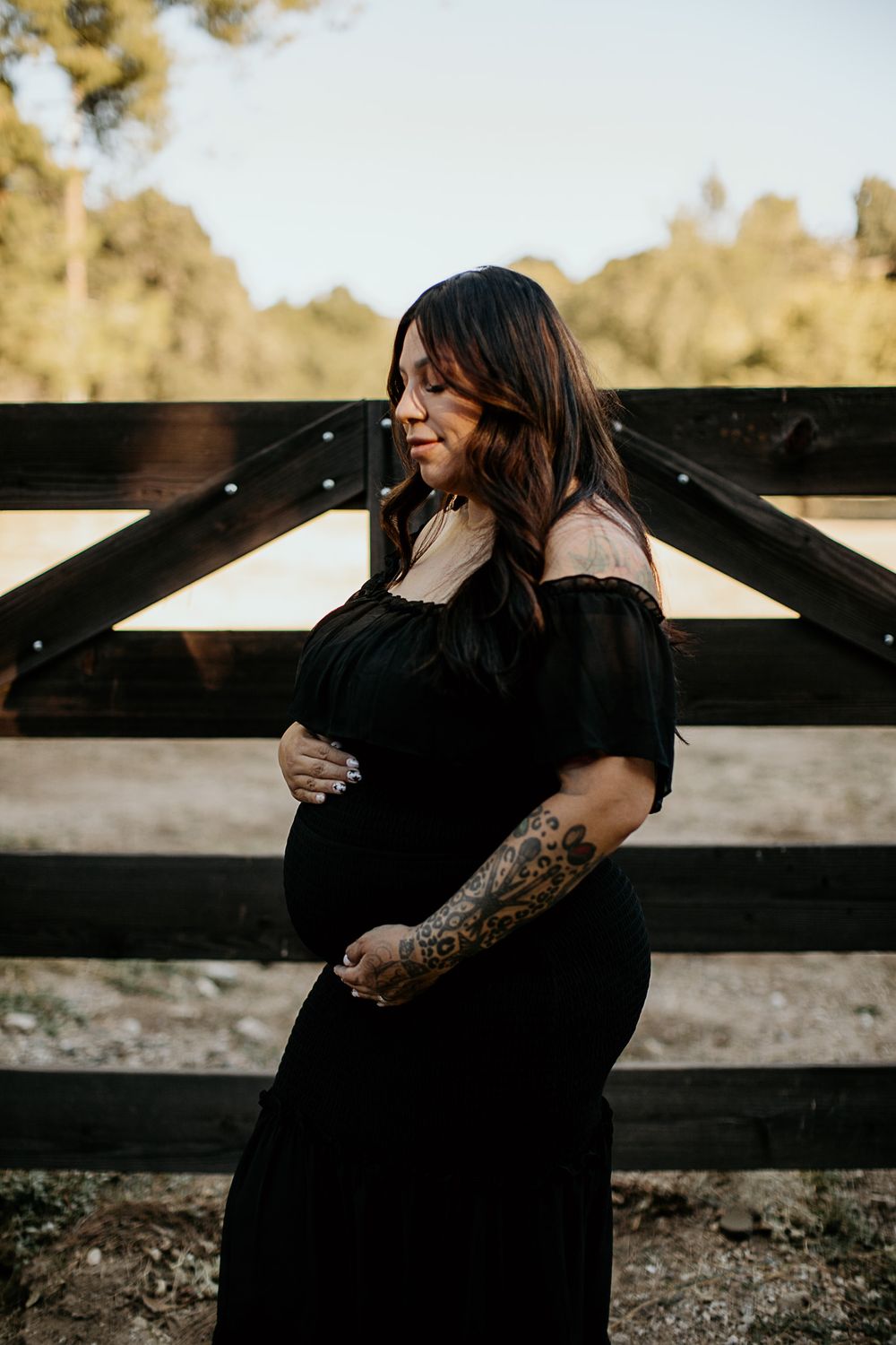 Outdoor maternity photoshoot by rustic wooden fence at sunset.