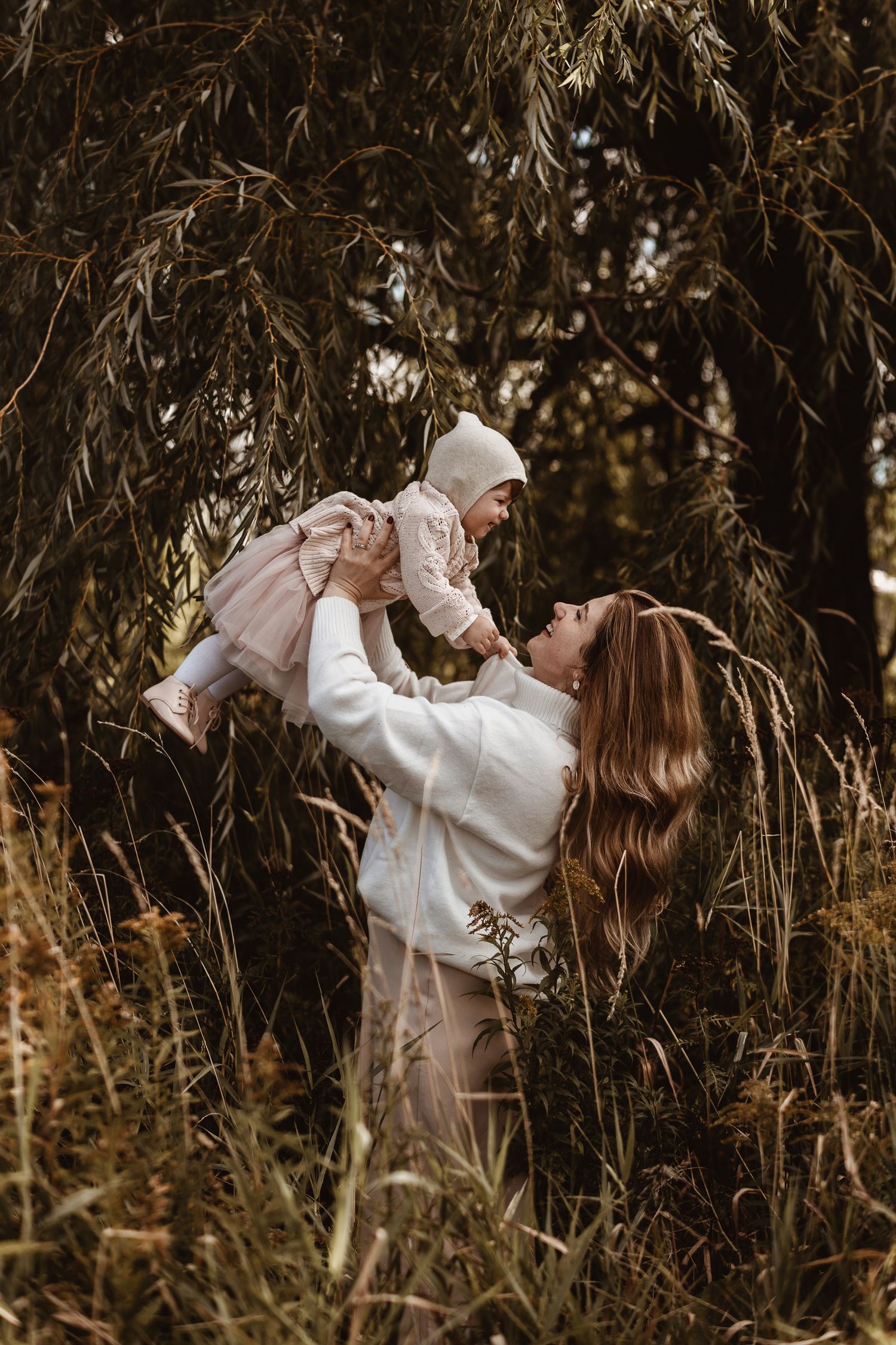 Joyful outdoor family moment captured under hanging willow branches.