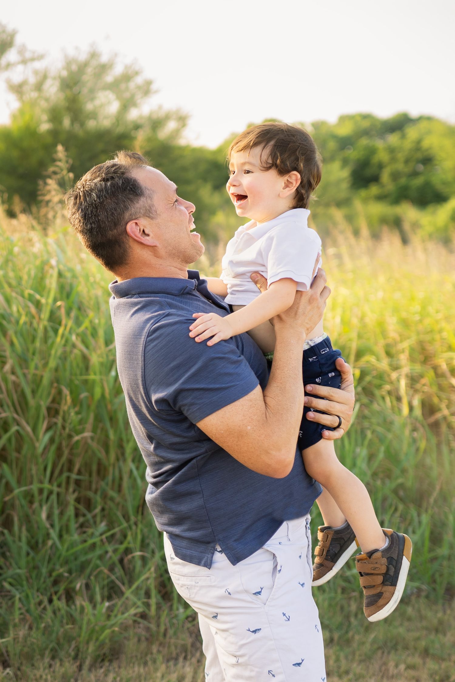 dad wearing blue polo shirt holding toddler son in white shirt and blue shorts