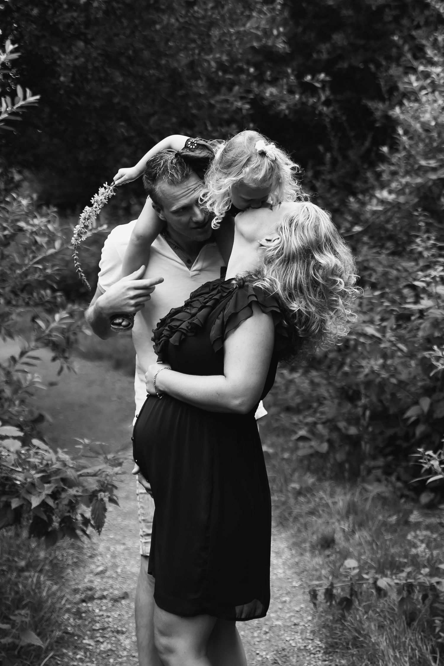 A couple shares an intimate moment on a nature path in black and white.