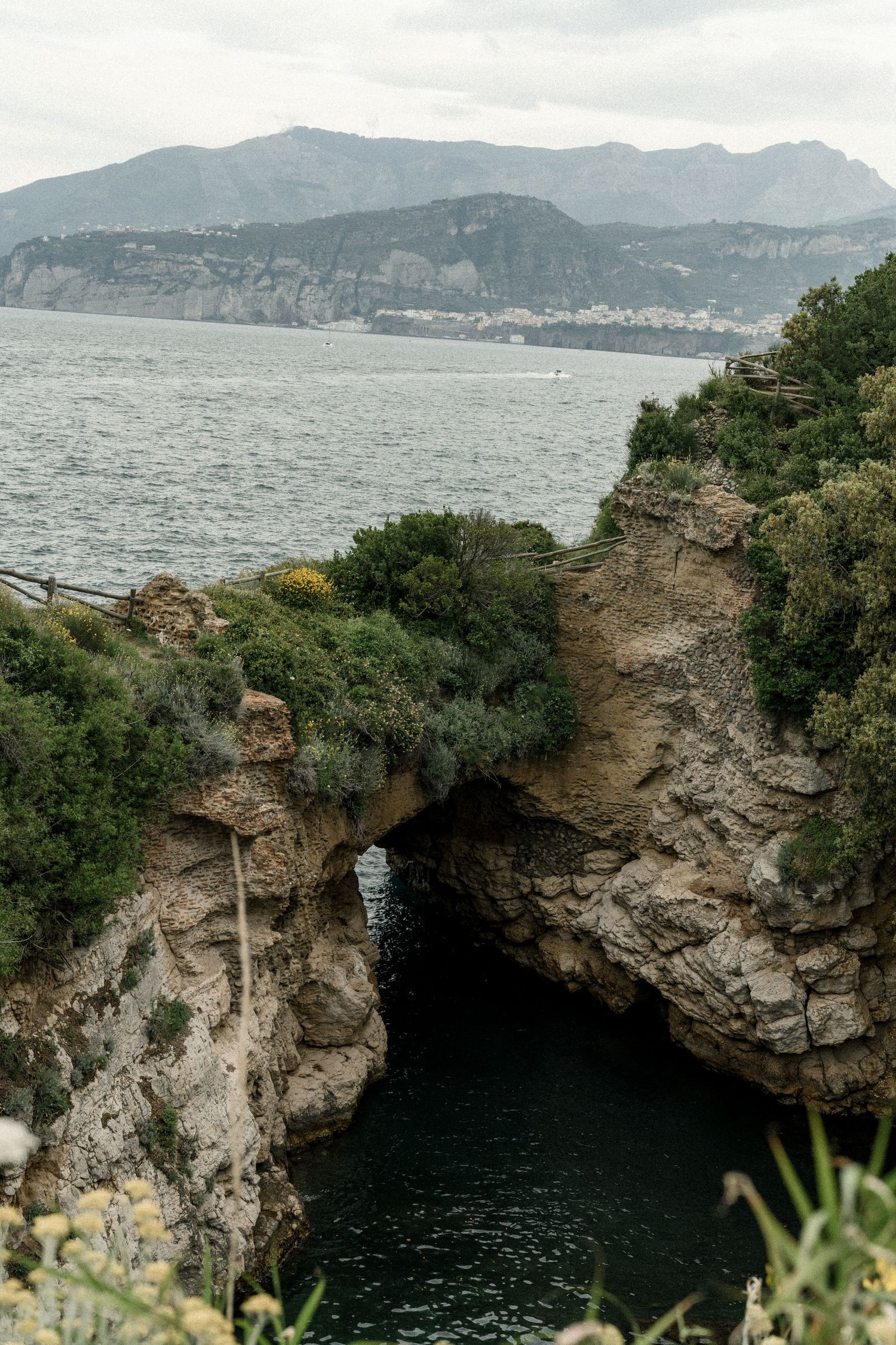 A scenic natural stone arch formation over ocean waters with mountains in the distance.