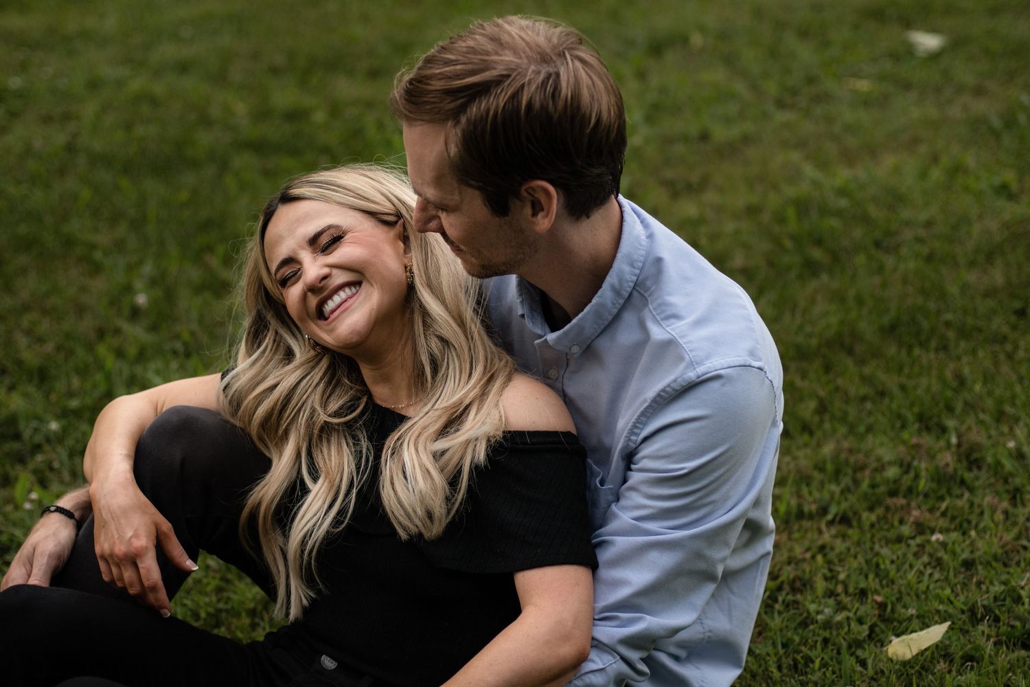 Couple shares playful moment while relaxing on grass outdoors.
