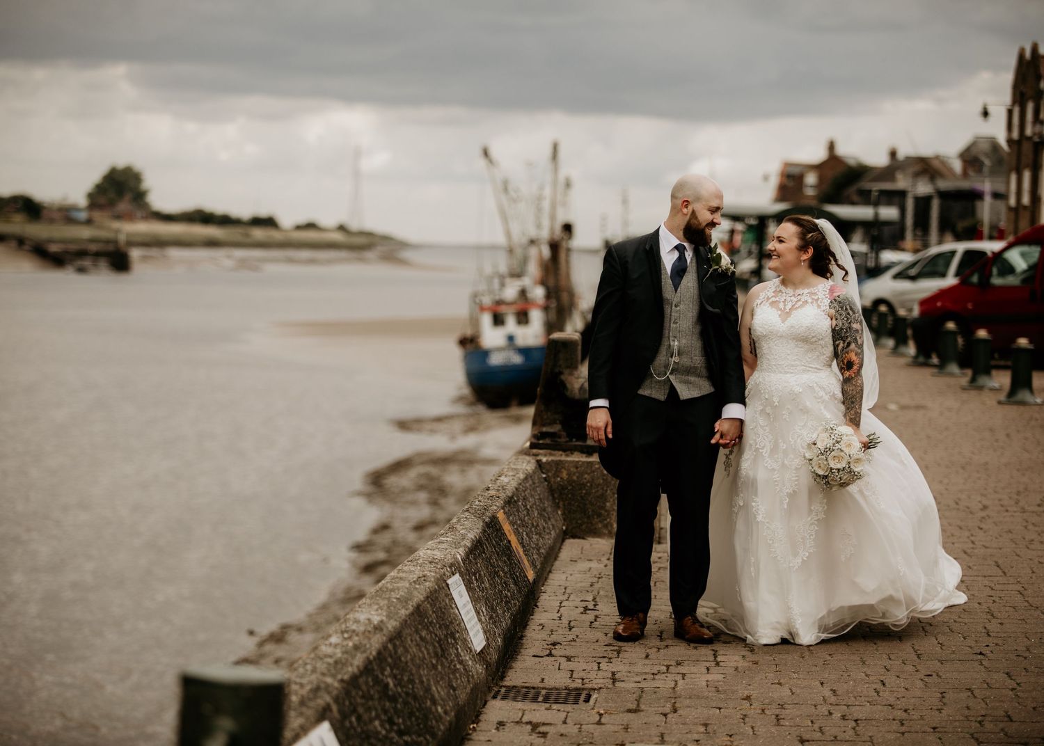 couple holding hand next to kings Lynn docks with boats behind