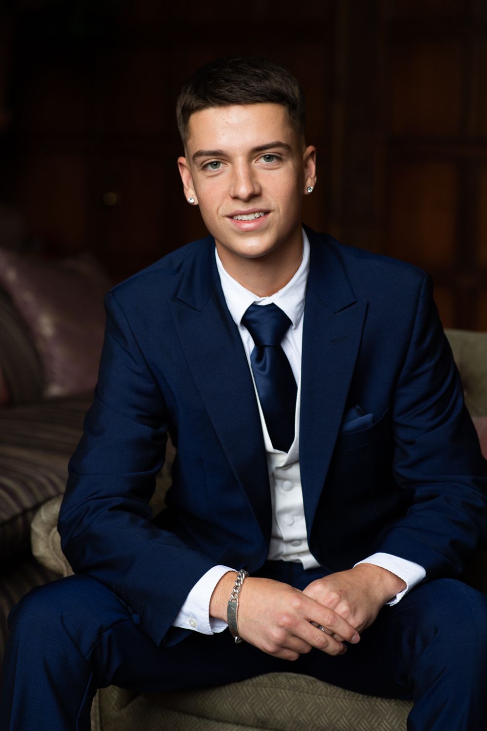 A formal portrait in a navy suit and tie against a dark interior background.