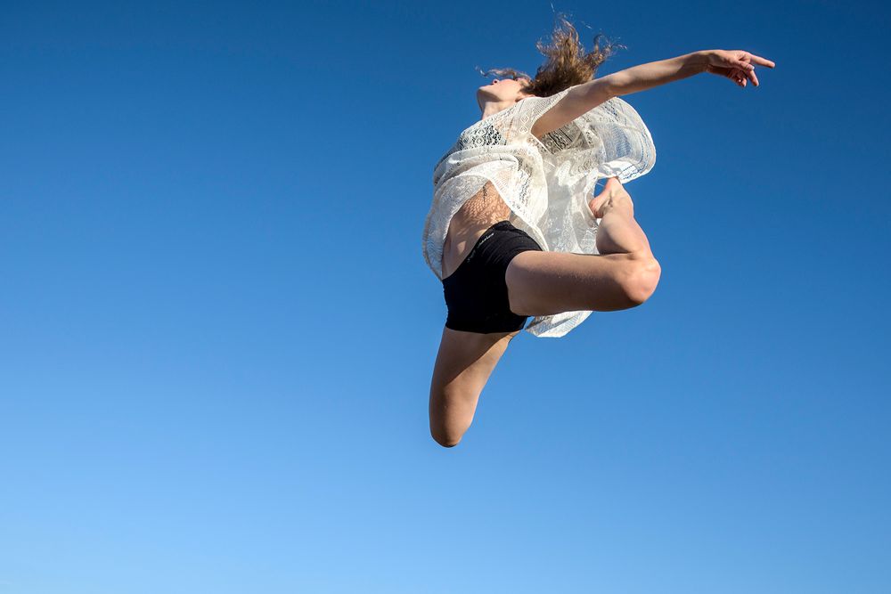 danseres Sandrine Wouters hoog springend in de lucht met blauwe achtergrond