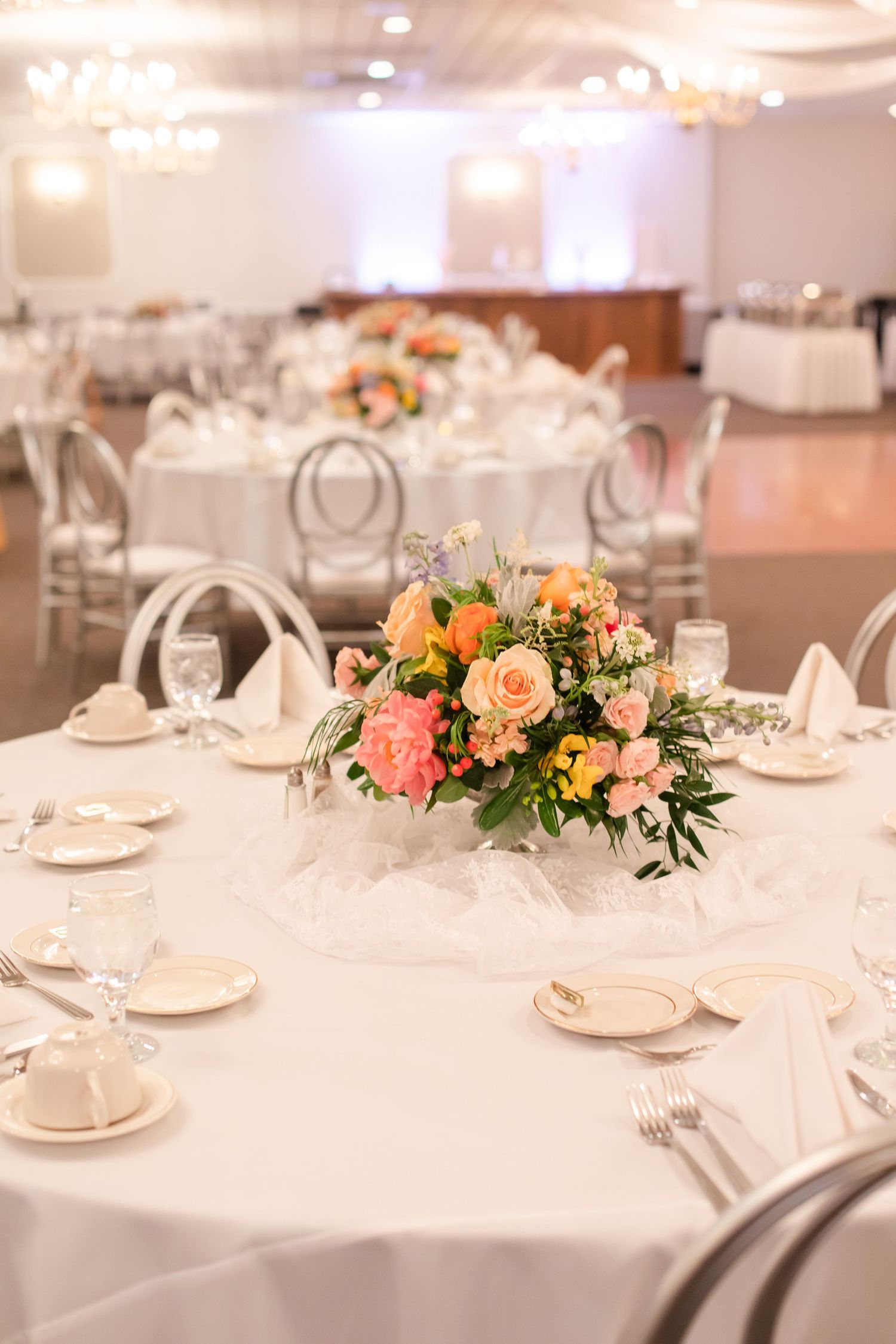 Elegant wedding reception room with white tables and peach floral centerpieces.