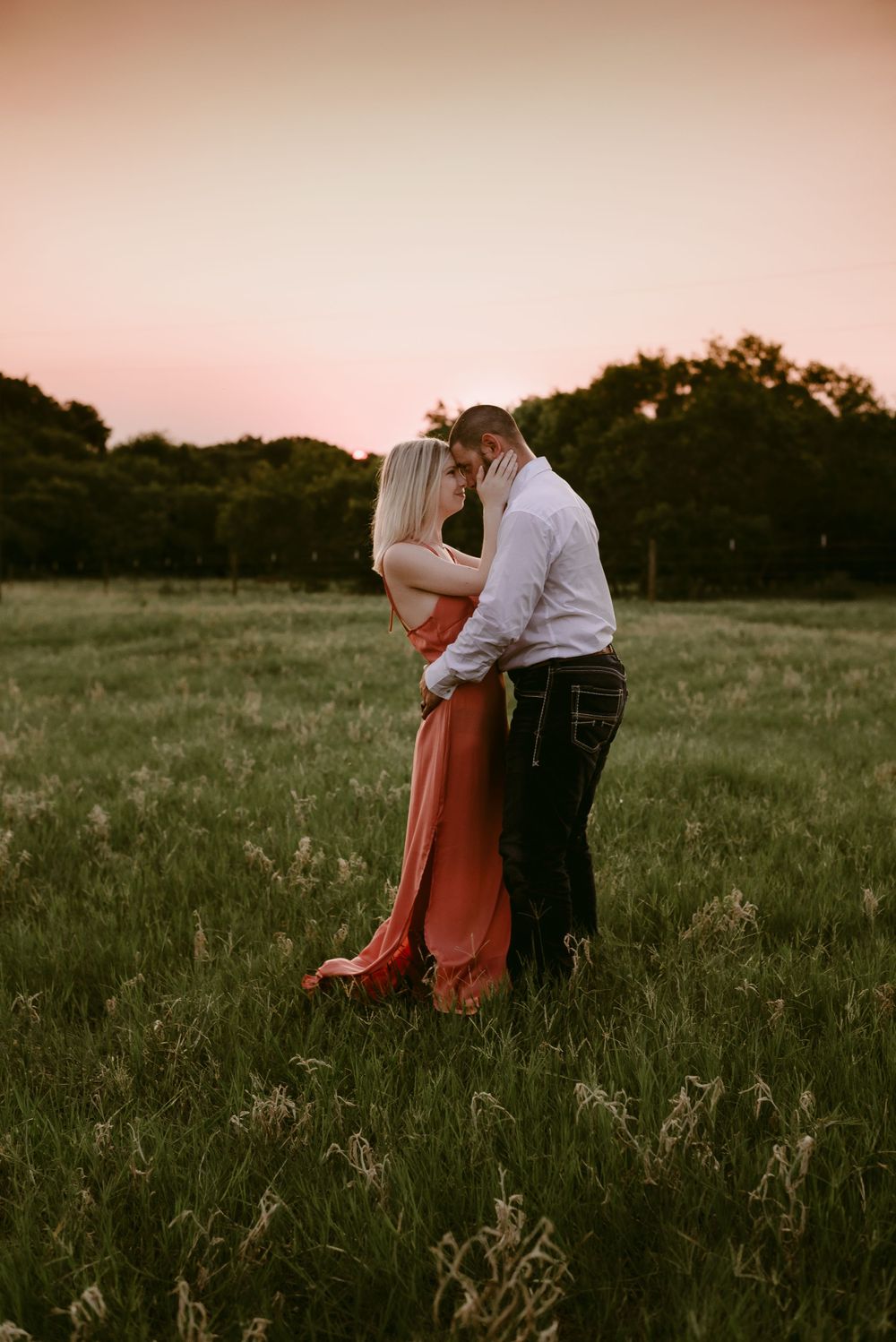 Romantic couple embracing in a meadow during golden hour sunset.