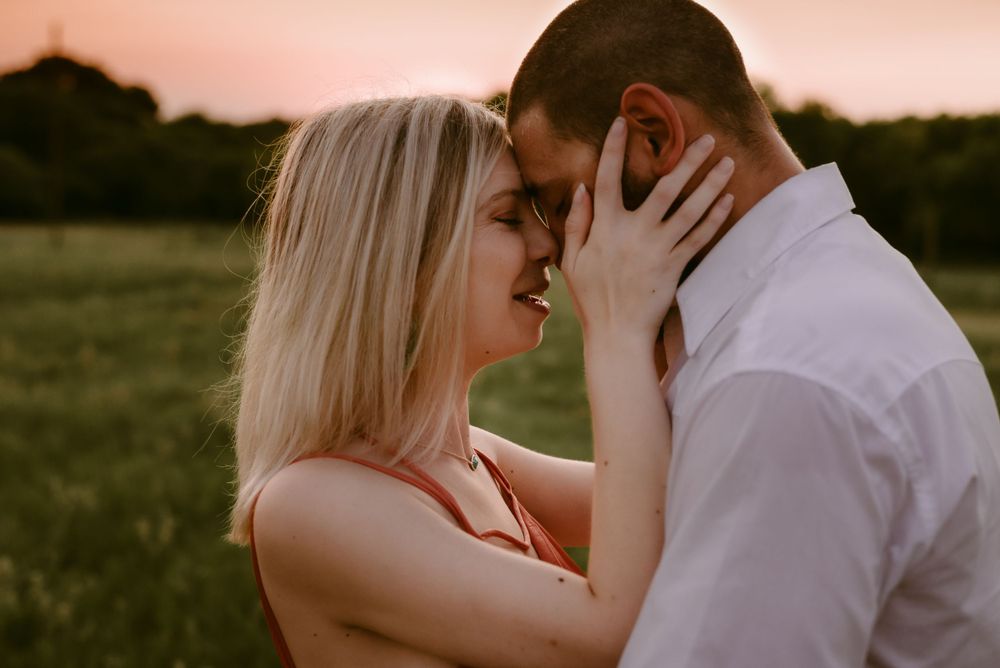 Intimate moment shared between a couple in a sunlit field at dusk.