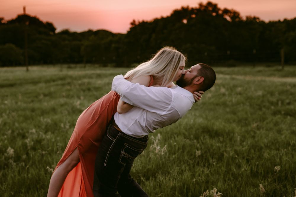 Playful couple sharing a dip pose in a field at sunset.