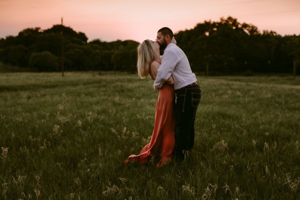 Couple sharing an intimate moment in a grassy field at dusk.
