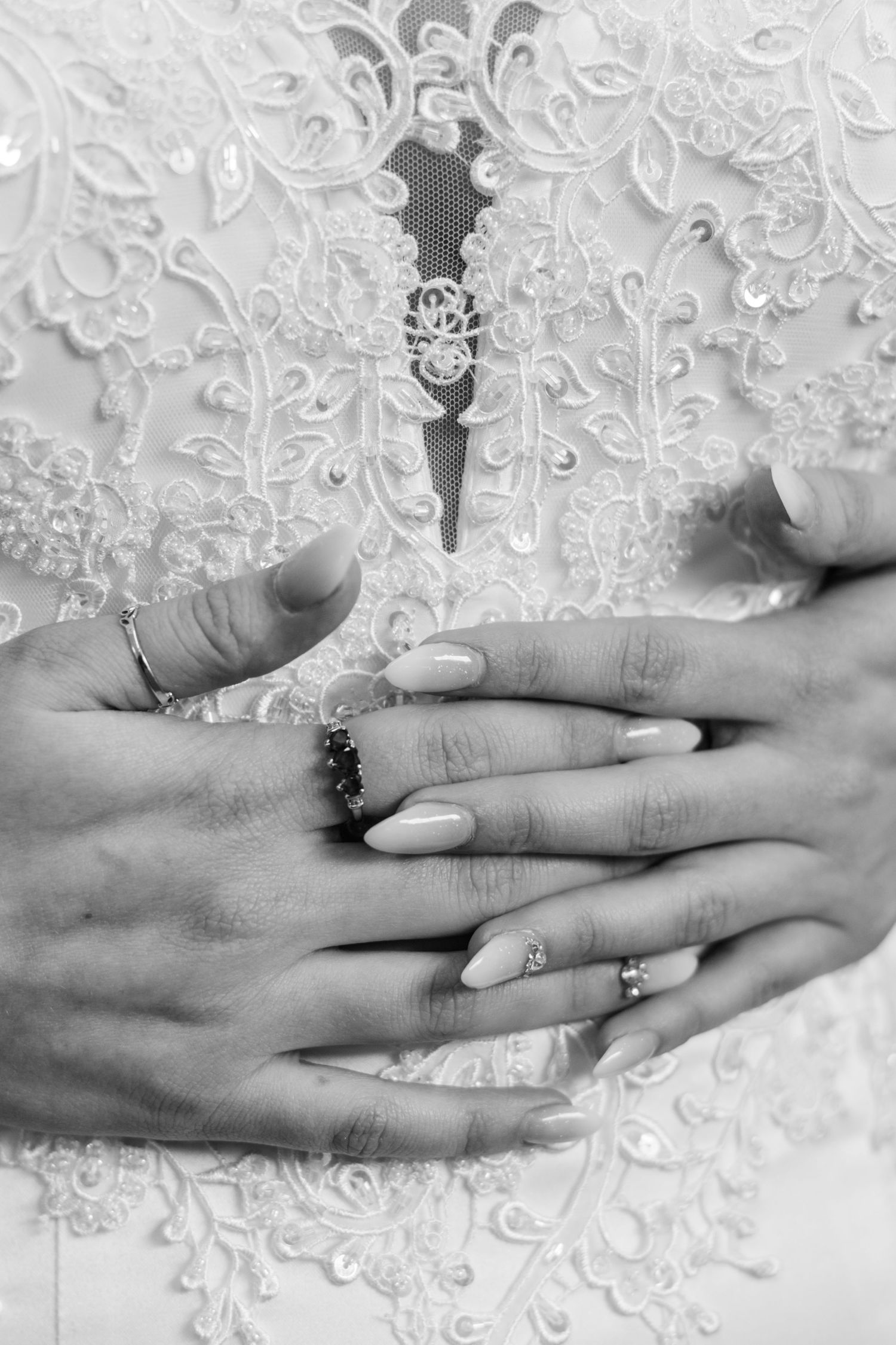 Black and white photo of hands with engagement rings against lace wedding dress fabric.