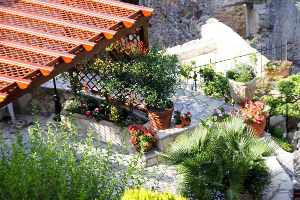 Mediterranean garden terrace with terracotta roof tiles and colorful potted flowers.
