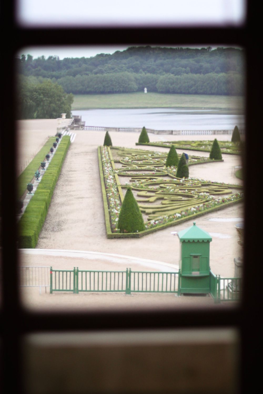 Formal French garden with geometric patterns and manicured hedges viewed through a window.