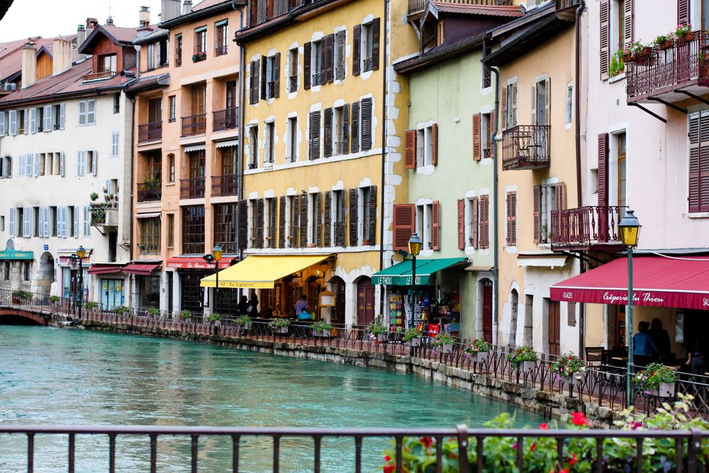 Colorful buildings with restaurants line a turquoise canal in Annecy's historic old town.