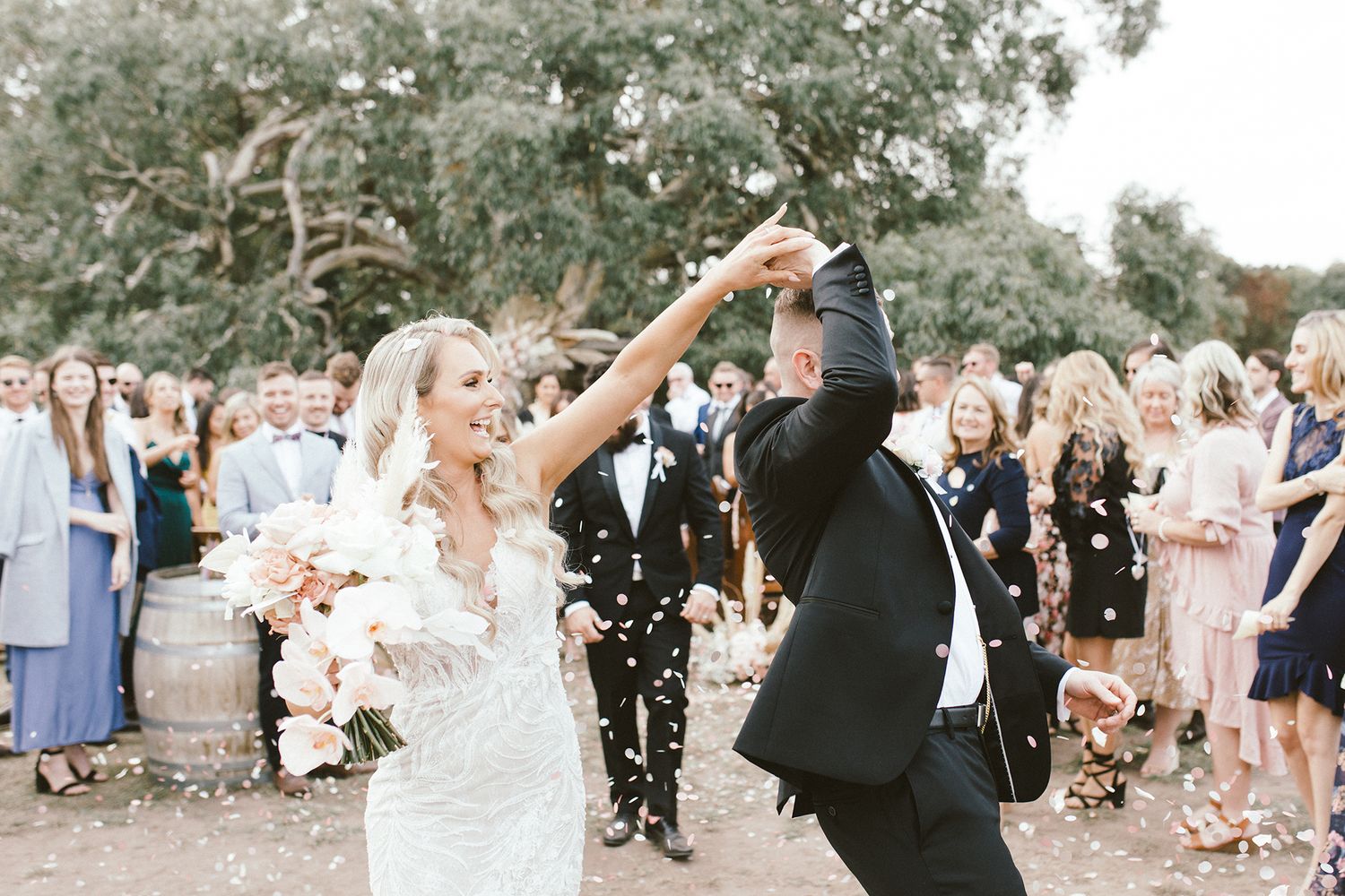 A romantic outdoor wedding celebration with confetti being tossed as a couple dances joyfully among wedding guests.