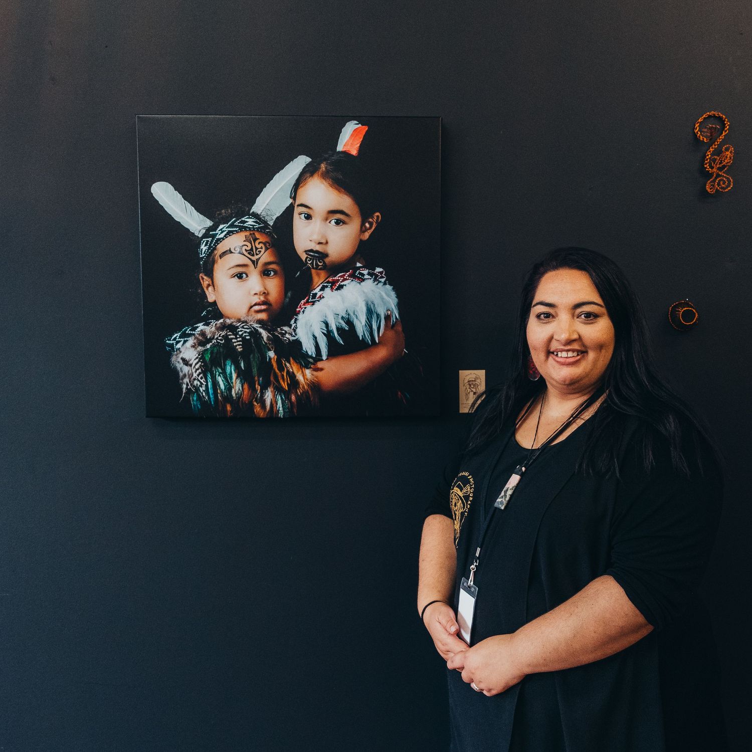 Maania Tealei standing next to photo she took of her children styled as Maori Portraits at an exhibition in Timaru, NZ