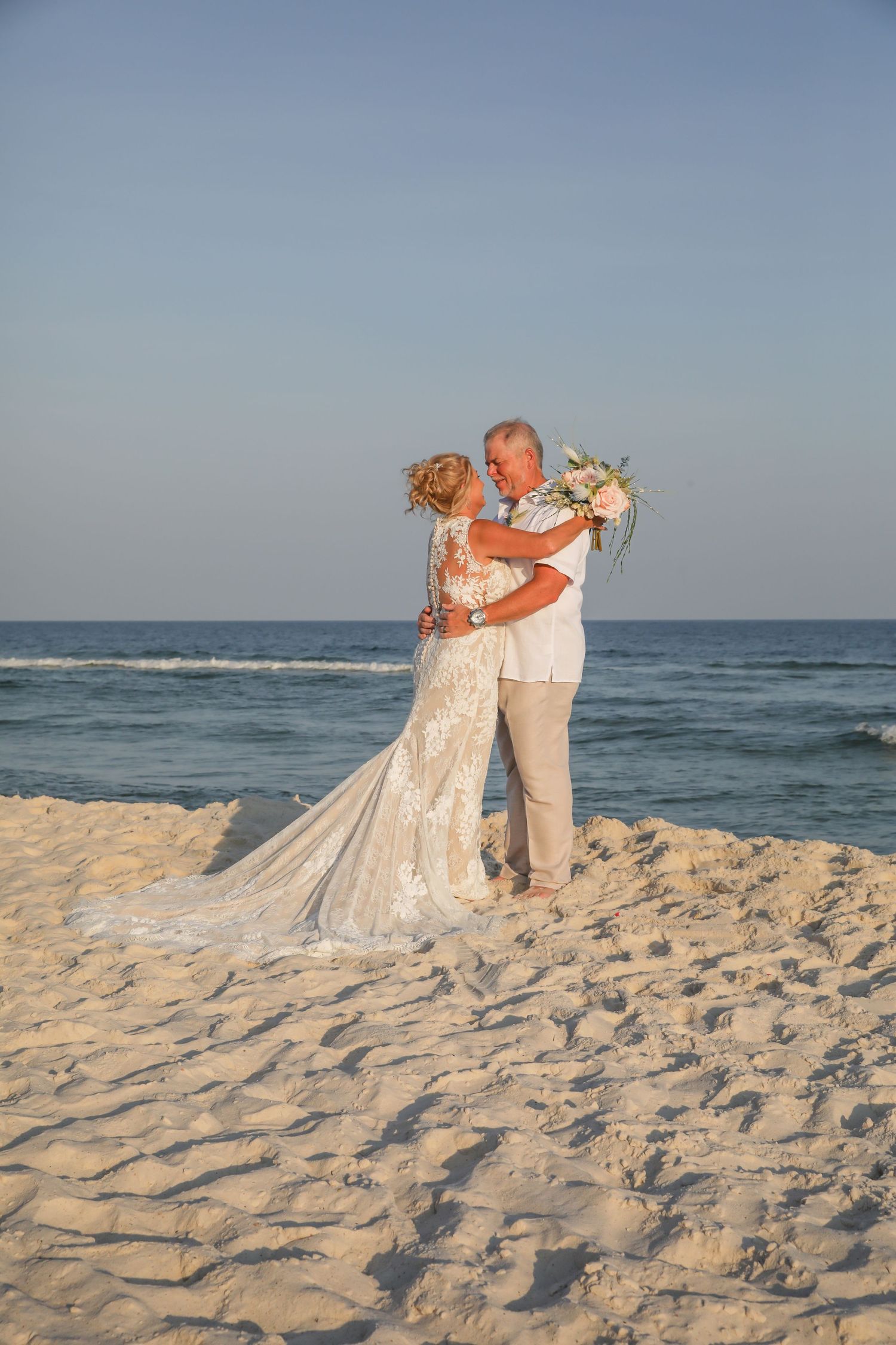 A newlywed couple embraces on a sandy beach during their coastal wedding ceremony.