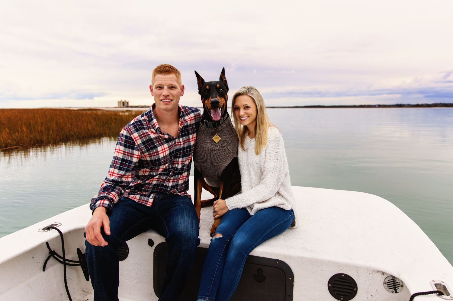 Couple sitting with their black dog on white boat in marsh waterway.