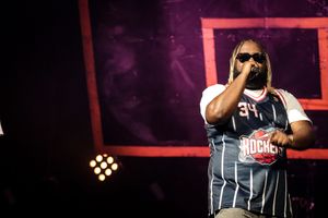 Concert performer in athletic jersey style outfit on stage with red lighting.