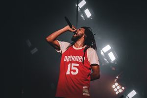 Artist in red sports jersey performs under dramatic stage lighting with floating money effects.