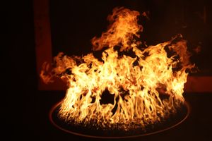 A dramatic circular fire display with intense orange flames against a dark background.