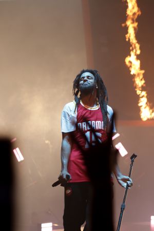 Concert performer in red sports jersey with fire effects in background during live show.