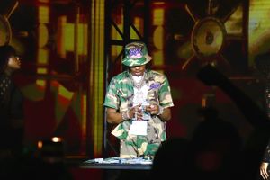 Concert performer wearing a bucket hat and camo outfit on stage with orange lighting effects.
