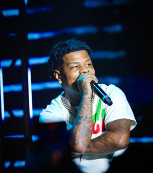 Performer in white shirt singing into microphone with blue stage lighting in background.