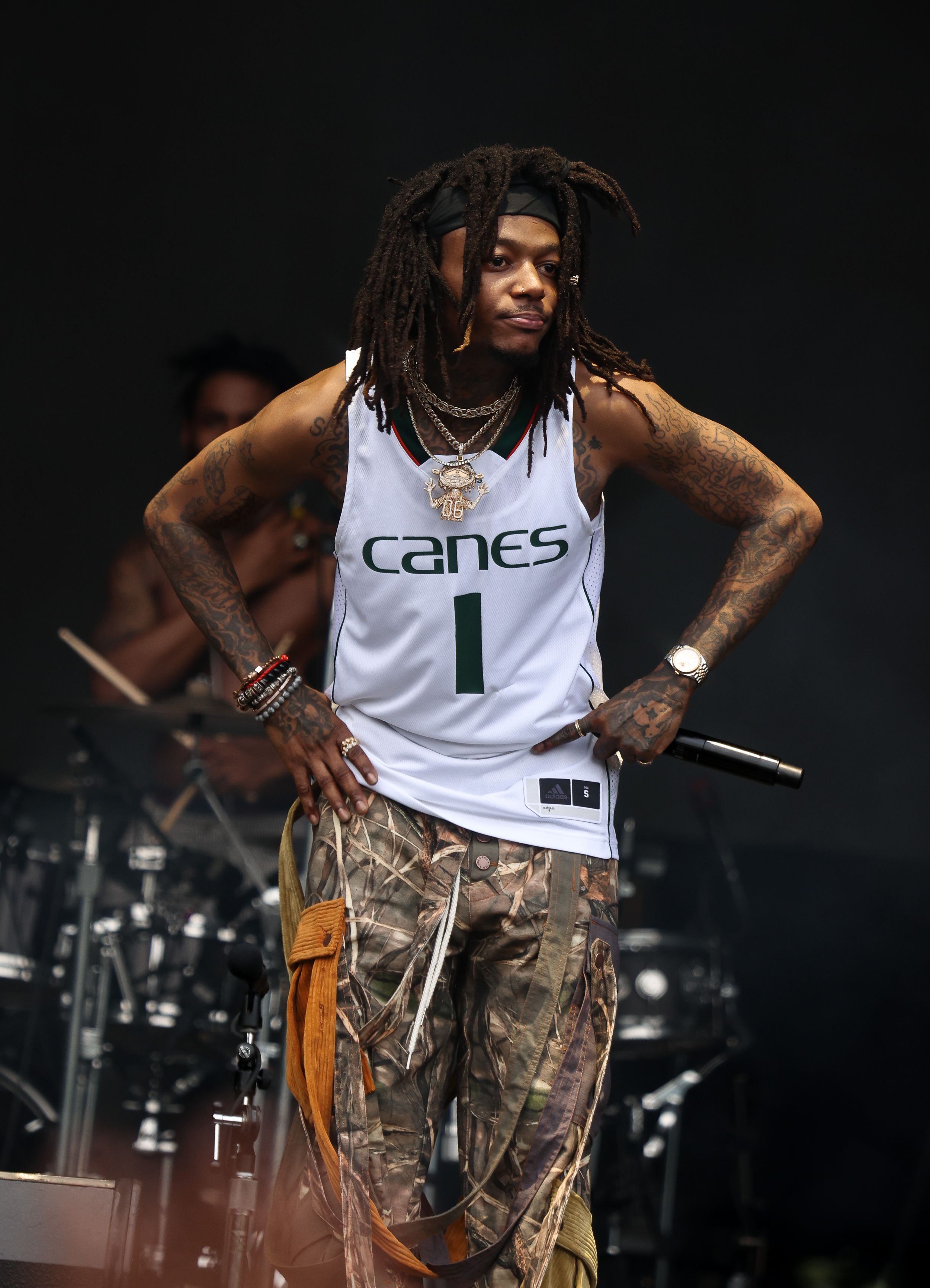 Performer wearing Canes basketball jersey and camo pants on concert stage.