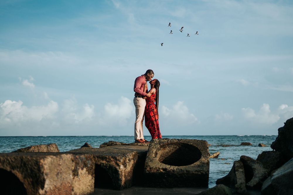 A couple embraces on rocky coastal cliffs with birds flying overhead.