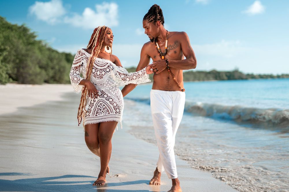 A couple walks hand-in-hand along a tropical beach shore in summer attire.