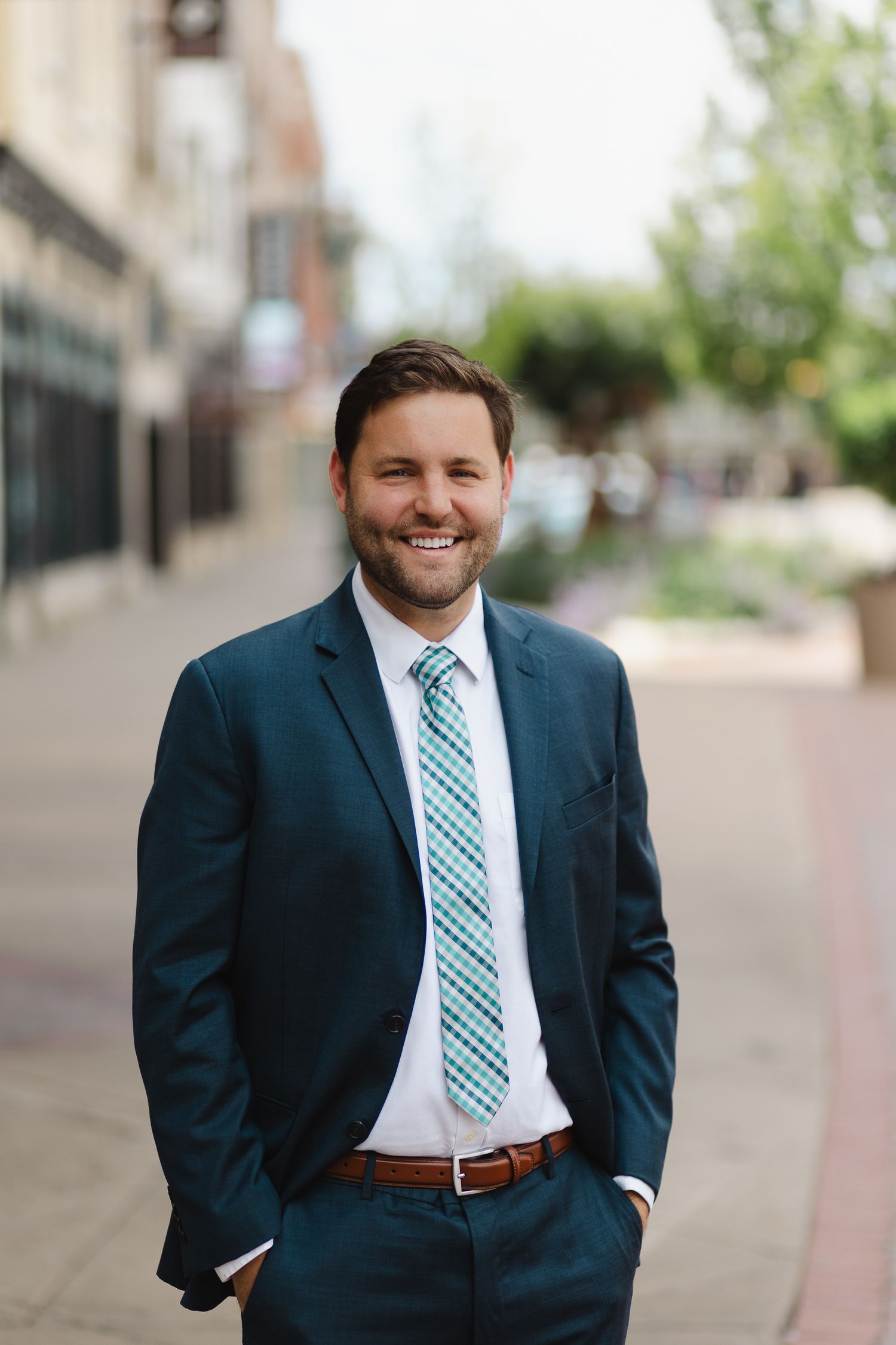 Corporate headshot of a man in a navy suit on a city street, by Konrad Odhiambo.