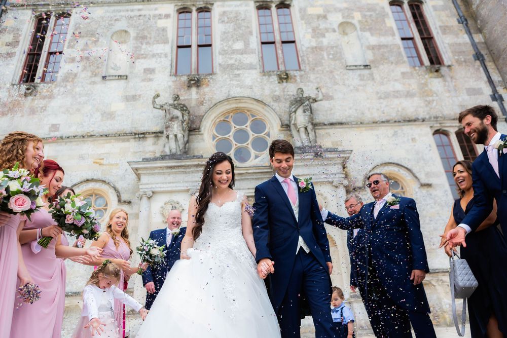 Newlyweds celebrate with confetti outside historic stone church with wedding party.