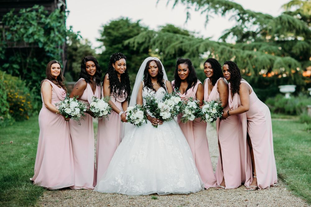 Bridal party in pink dresses and white gowns pose with bouquets in garden setting.