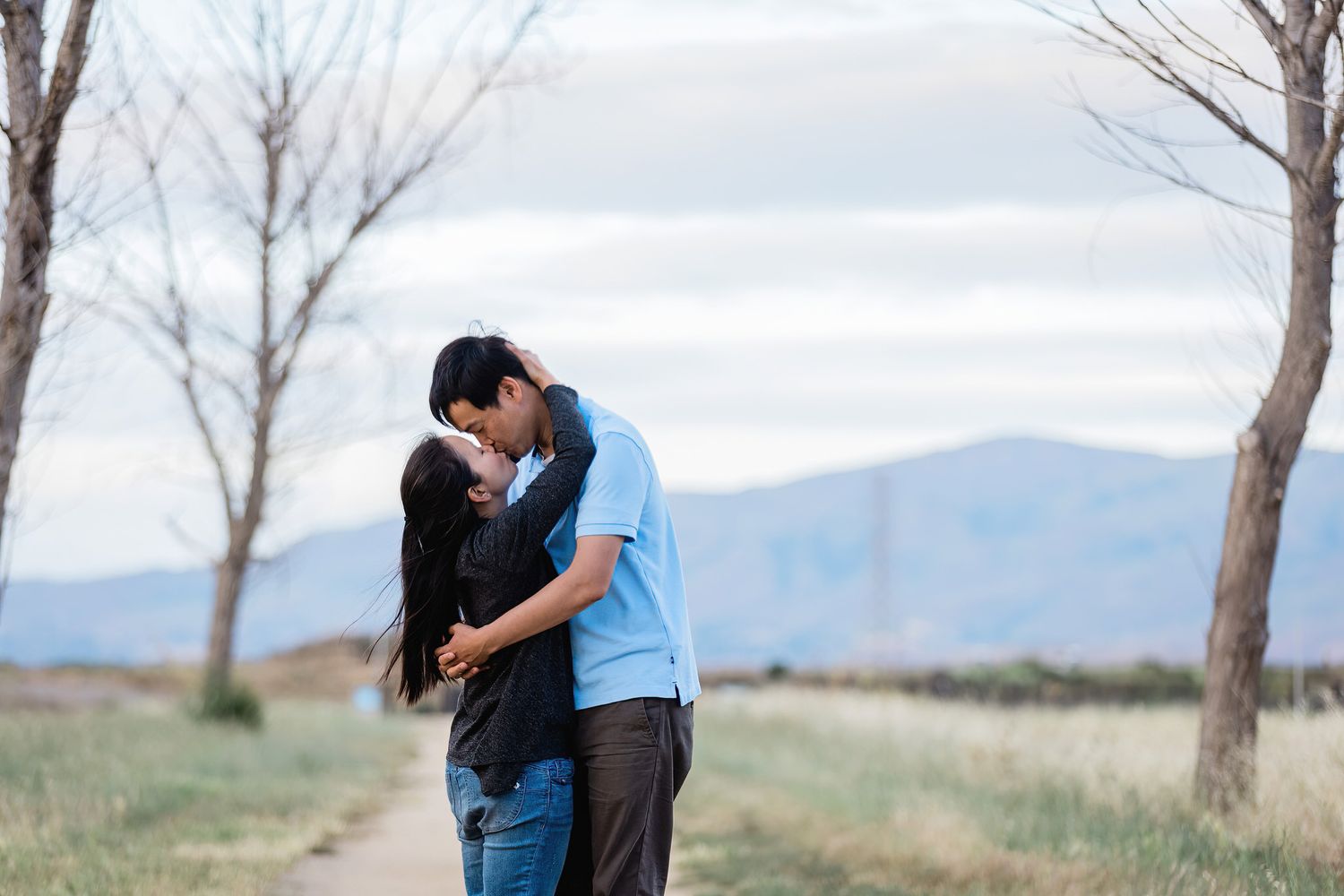 Romantic couple sharing an intimate moment on a path with mountain views.