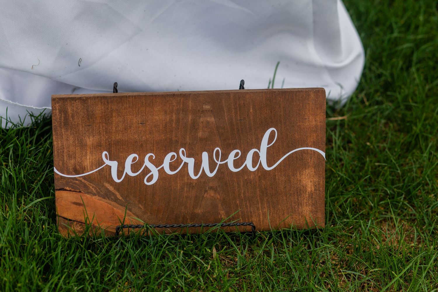 A rustic wooden reserved sign placed on grass for wedding seating.