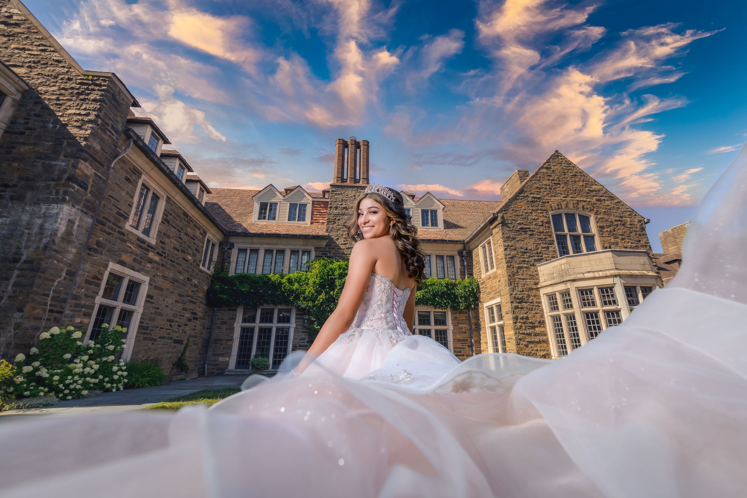 A pink ballgown photographed against a stone building exterior during golden hour sunset.