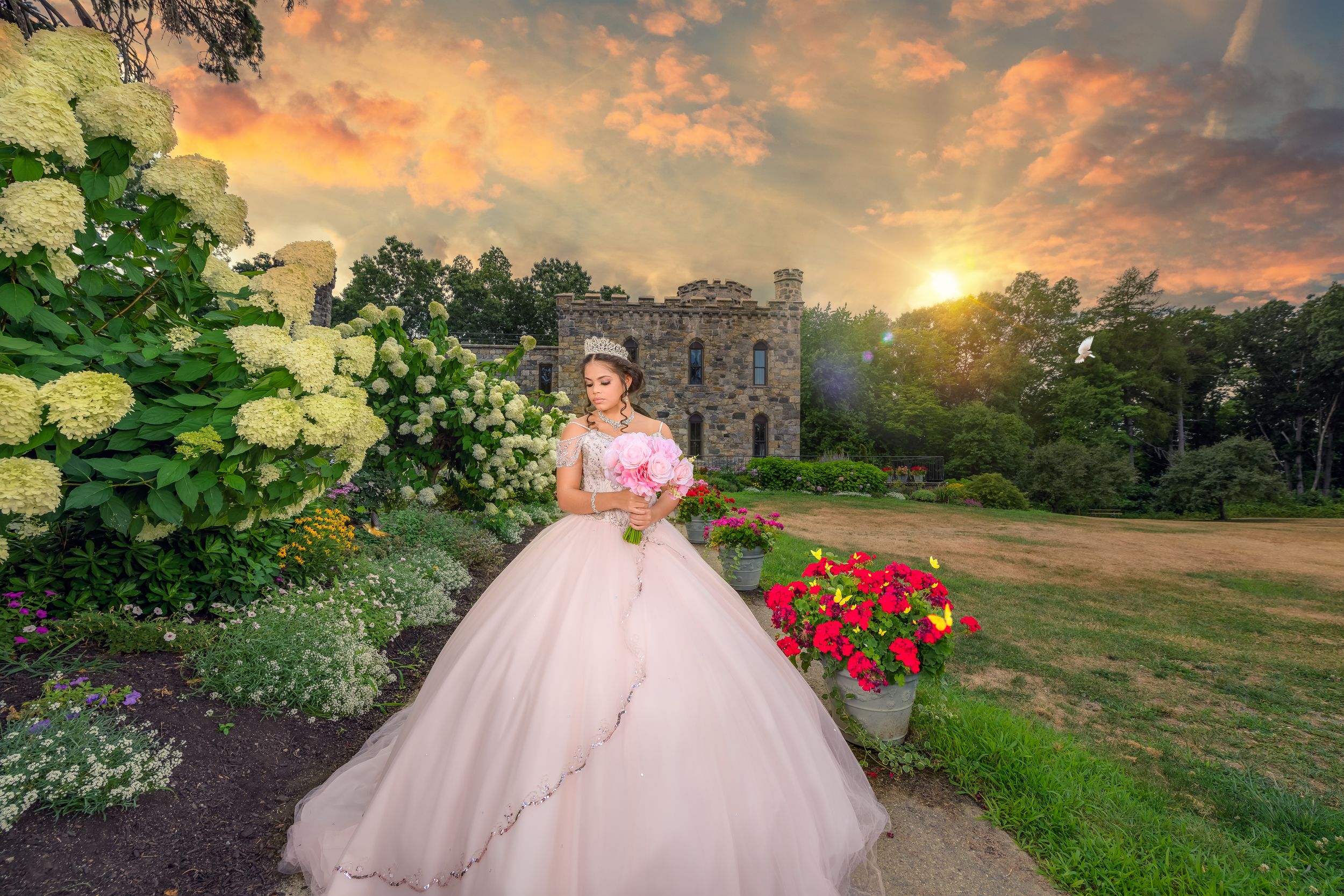 Pink princess ballgown photographed in a garden setting with red flowers at sunset.