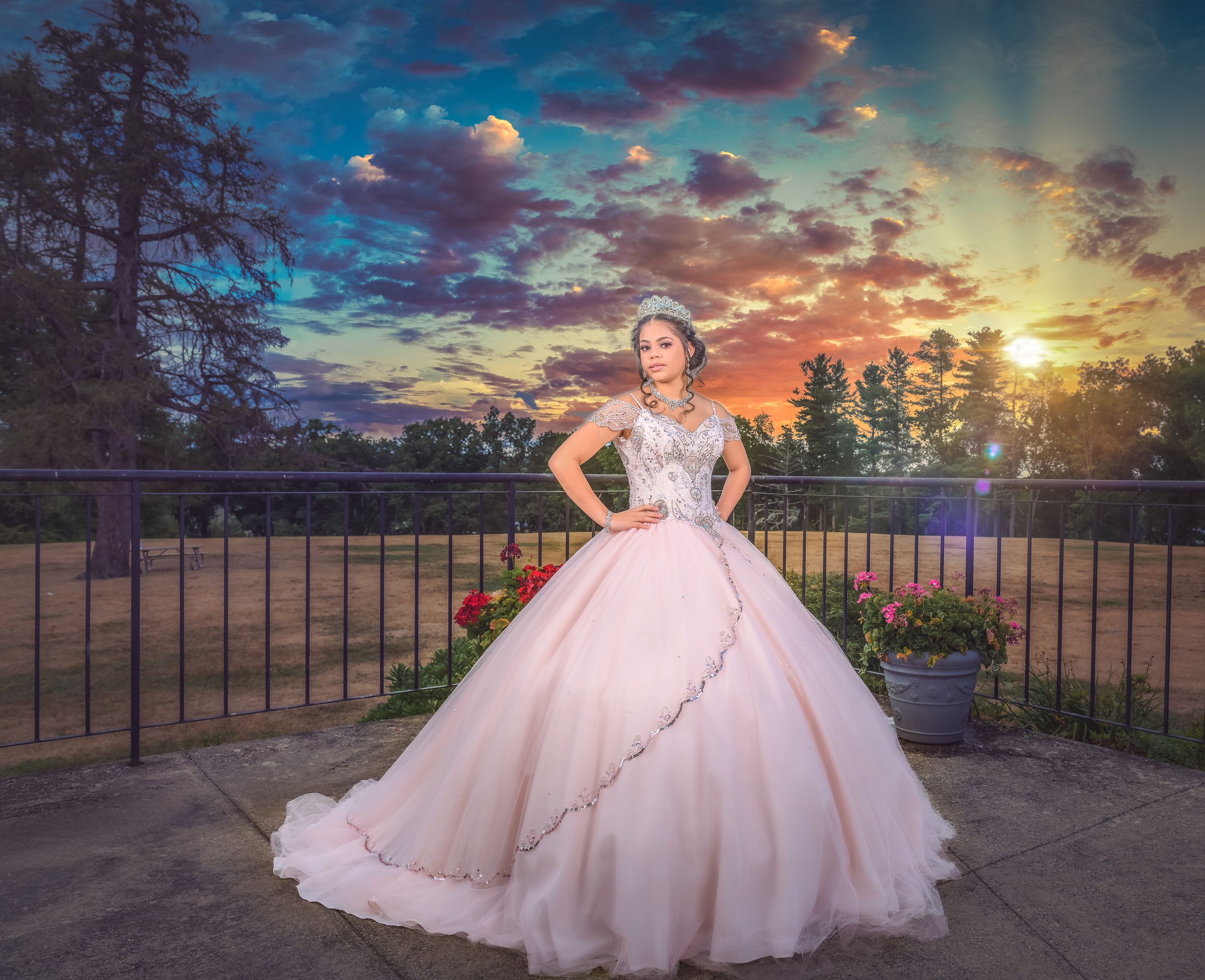 Pink ballgown dress photographed against a dramatic sunset sky with blue clouds.