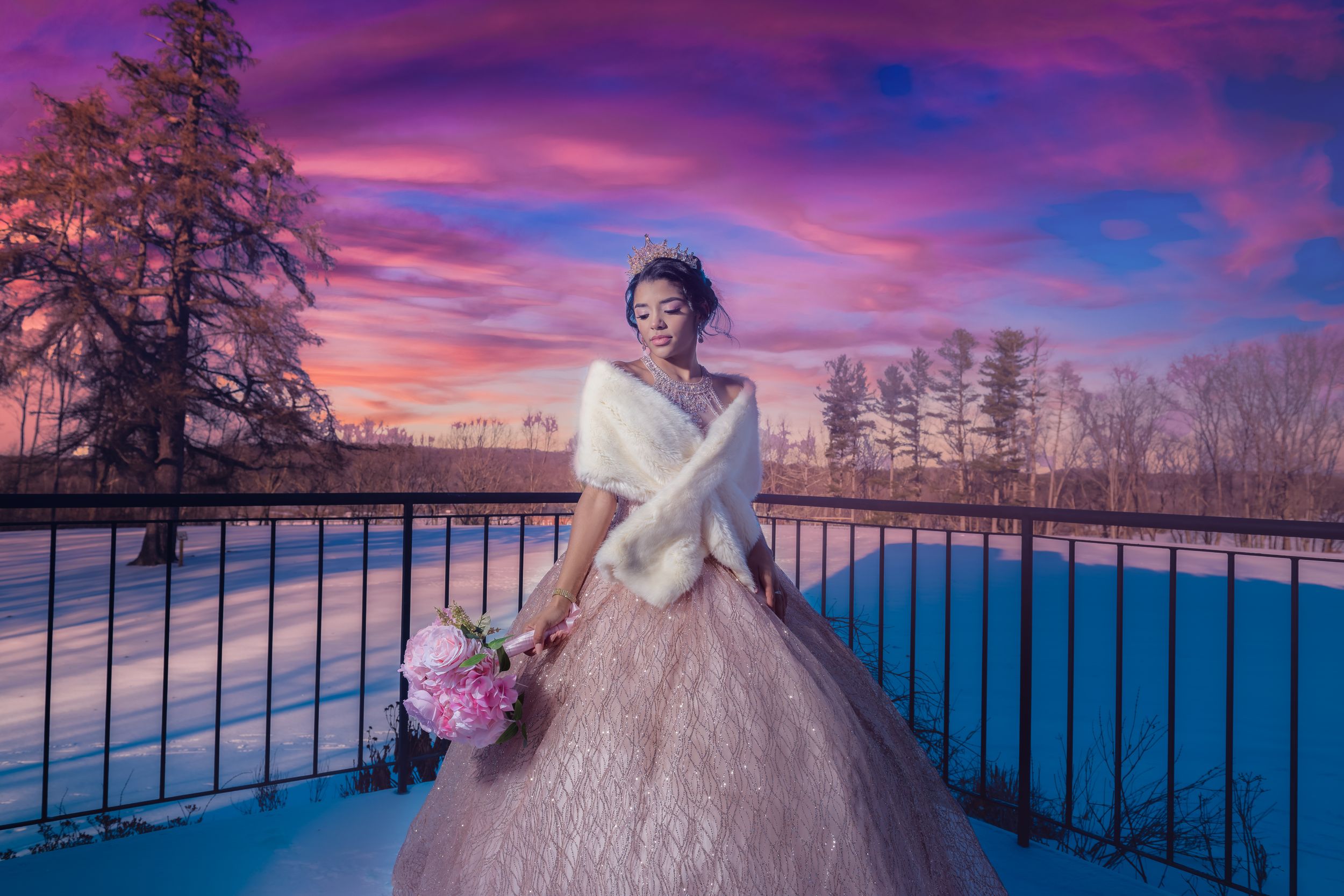Pink ballgown photographed against a vibrant purple and pink sunset over water.