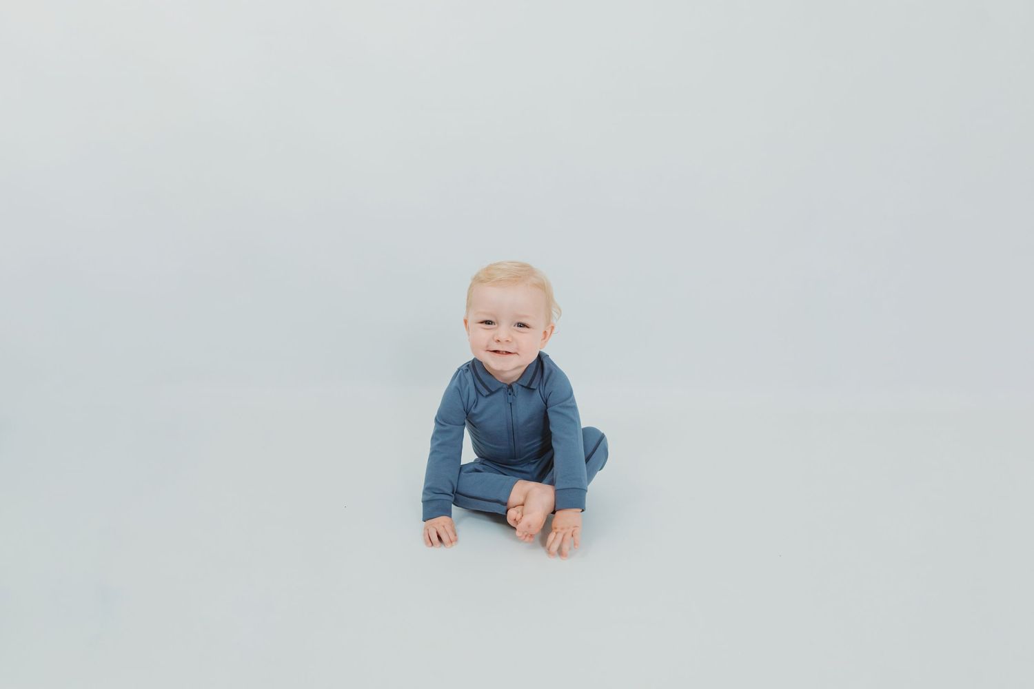 Baby in denim outfit sits on light gray backdrop during studio photo session.