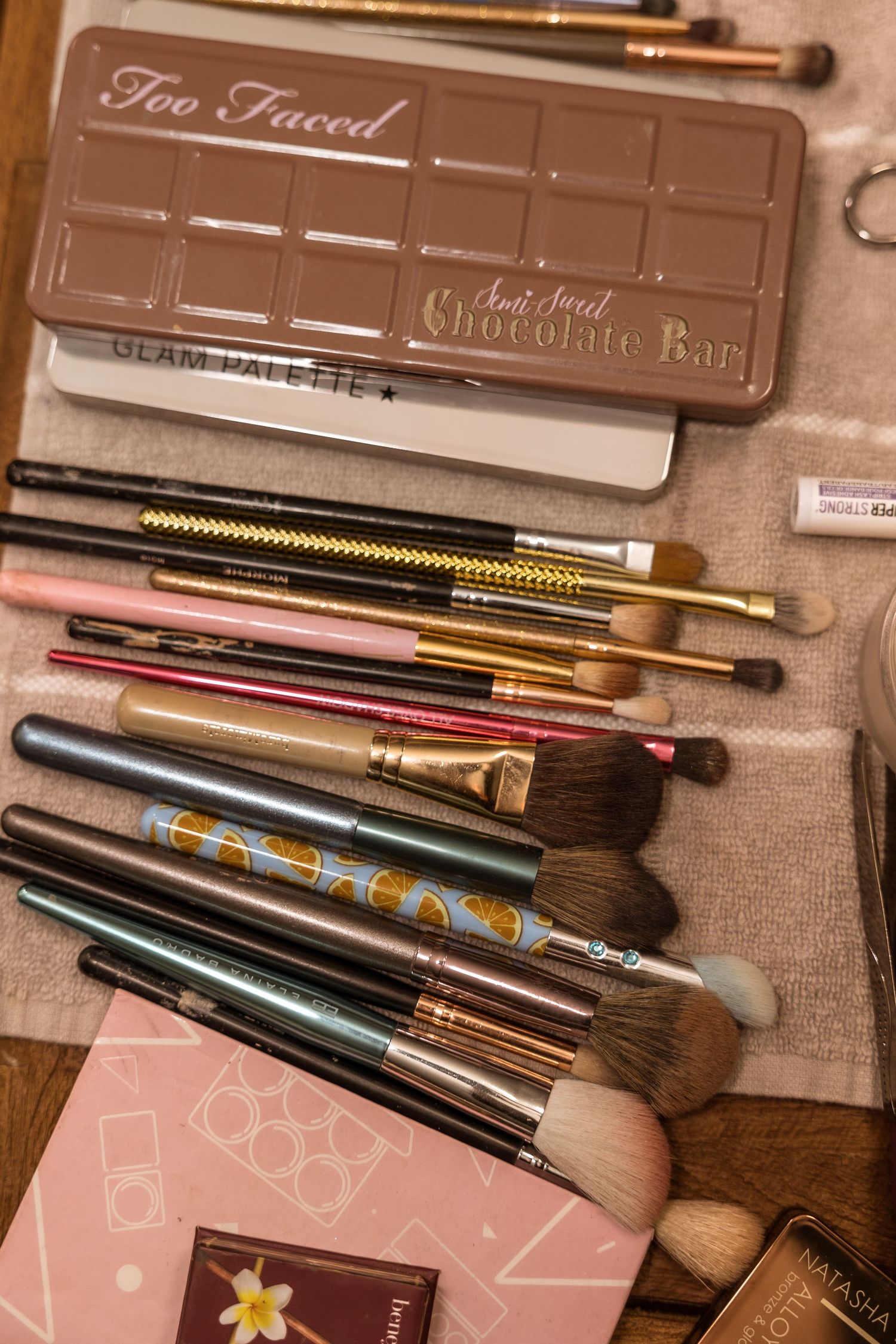 Too Faced chocolate palette with collection of makeup brushes arranged on beige surface.